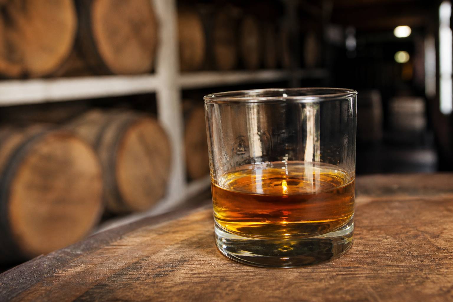 Verre tumbler de whisky ambre single malt sur fond de futs de chene dans une distillerie